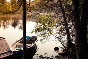 Boat on the pier in a beautiful forest lake that illuminates the setting sun