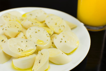 Palm hearts in a white plate in a black table with a cup of orange juice in the background