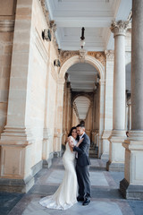 Obraz premium Fashion photo. Young elegant sexy couple hugs, wearing suit and white dress with a train, enjoy their honeymoon, luxury style, love, stylish lovers. Love story. Lifestyle concept.