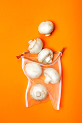 Cute organic champignons in the eco bag on a trendy orange background. Zero waste concept, plastic-free, eco-friendly shopping, vegan