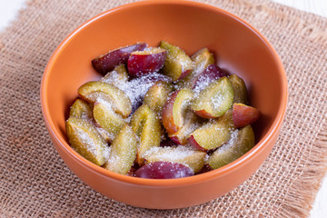 Sliced plums in a bowl with sugar