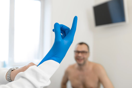 urologist doctor puts on medical gloves before examining a patient who is waiting on a couch