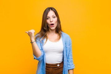 young pretty woman looking astonished in disbelief, pointing at object on the side and saying wow,...