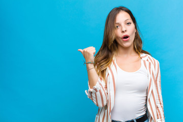 young pretty woman looking astonished in disbelief, pointing at object on the side and saying wow,...