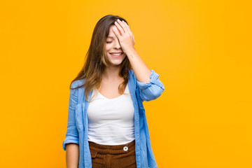 young pretty woman laughing and slapping forehead like saying d‚Äôoh! I forgot or that was a...