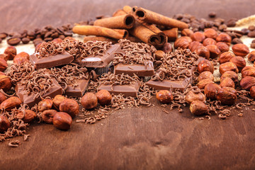 Chocolate tiles, cinnamon and nuts on a wooden background
