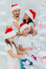 Friendly family is decorating Christmas tree with joy. They are looking at each other and laughing