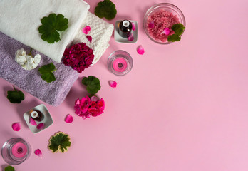 SPA care using essential oils and sea salt. Geranium essential oil, geranium flowers and leaves, pink sea salt, candles and towels on pink background.