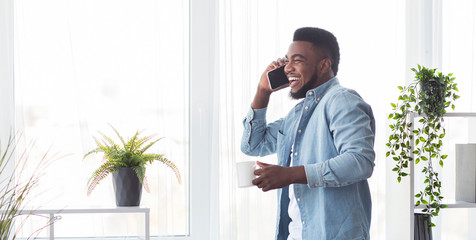 Young cheerful businessman talking on phone and holding coffee cup