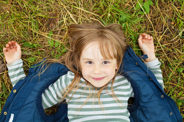 top view portrait of a pretty child girl in blue jacket relaxing on a grass