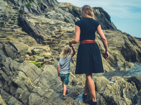 Young mother and toddler walking on rocks by the beach