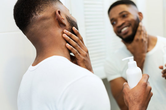 Young black man applying moisturizer on beard in bathroom