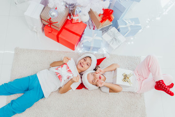 Obraz na płótnie Canvas Christmas Eve. Boy and girl of younger school age lie on a floor near the decorated Christmas tree