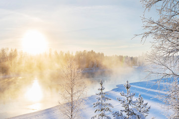 Mist over freezing river on a sunny cold winter day. Trees covered with frost and snow.