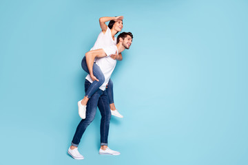 Full length body size profile side view of nice attractive cheerful dreamy couple piggybacking having fun looking watching vacation isolated on bright vivid shine vibrant blue turquoise background