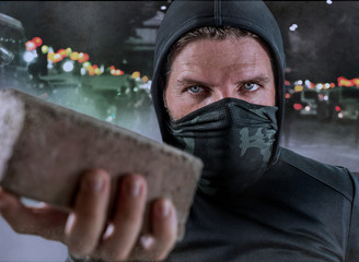 young man as ultra and radical anarchist rioter . furious antifa protester in face mask throwing...