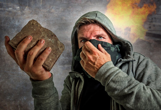 young man as ultra and radical anarchist rioter . furious antifa protester in face mask throwing brick hostile on street on demonstration in violet riot and chaos
