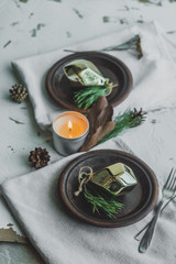 Christmas and New Year table setting in rustic style with handmade details. Dining place decorated with handmade dishes, pine cones, branches and golden christmas decorations 