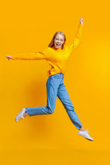 Fototapeta na wymiar Jumping millennial girl in the air over orange studio background
