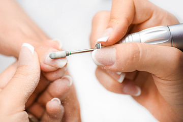 Une femme utilise une perceuse électrique pour lime à ongles dans un salon de beauté. Processus de manucure parfait des ongles ou opération en gros plan avec des débris volants éclatés.