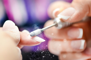 Manucure des ongles dans un salon de beauté femme. Perceuse à lime à ongles électrique en action, gros plan du doigt ou détail avec fond de couleur.