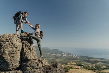 Young hiker an holding a woman hand helps to climb to the top of the mountain. The concept of help and support