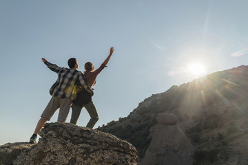 Back view of couple hikers standing on rock enjoying freedom raising hands up.