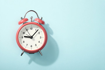 Red alarm clock with shadow lying on blue background. View from above.