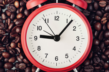 Red alarm clock lying on coffee beans. Seven minutes past nine on the clock. Concept of morning...