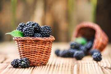Blackberries in wooden wicker basket. Fresh juicy forest fruits like a blackberry with leaf on rustic table.