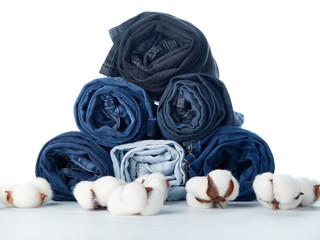 Fototapeta na wymiar Stack of rolled jeans and cotton flowers on light background