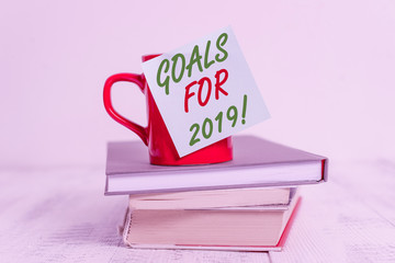 Conceptual hand writing showing Goals For 2019. Concept meaning object of demonstratings ambition or effort aim or desired result Coffee cup sticky note stacked books retro old retro wooden table