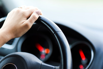 Woman hand holding steering wheel detail. Modern car dashboard with speedometer or tachometer in...