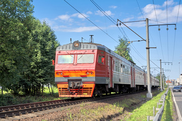 Obraz premium A red commuter train rides on rails on a summer sunny day. Public rail