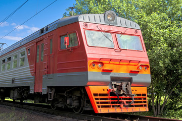 Fragment of a commuter train riding on metal rails on a sunny summer day