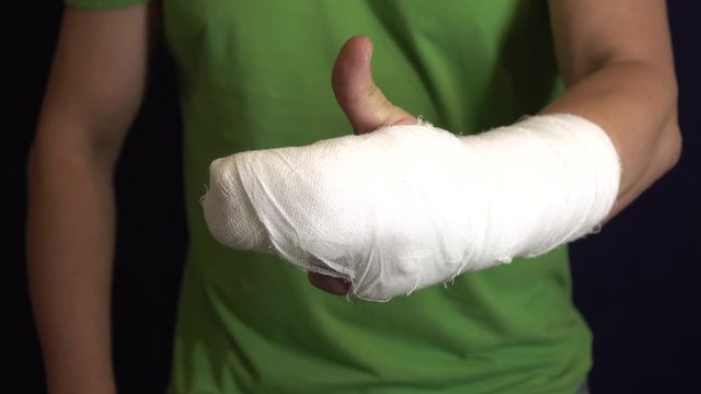 The man with the arm in a cast shows that everything is in order . Man's hand in bandages after surgery.