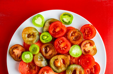 Sliced red, green and kumato tomatoes on white plate on red background