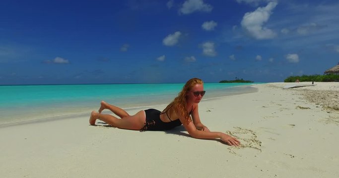 Blonde model lying and playing with sand on a beach in the Maldives 4K