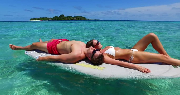 Young and attractive couple having some leisure time on top of a paddle board in an exotic beach in the Maldives 4K