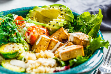 Buddha bowl with quinoa, tofu, avocado, sweet potato, brussels sprouts and tahini dressing. Healthy vegan food concept.