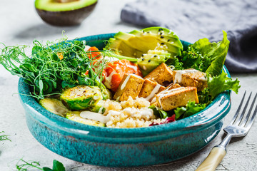 Buddha bowl with quinoa, tofu, avocado, sweet potato, brussels sprouts and tahini dressing. Healthy vegan food concept.