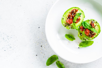 Stuffed avocado halves with sun-dried tomatoes and basil on white plate, top view. Healthy vegan food concept.