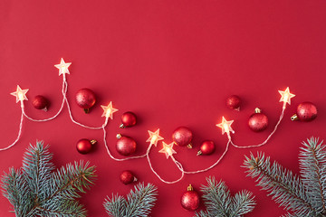 Flat lay frame with christmas garland, red christmas balls and spruce branches on a red background