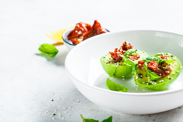 Stuffed avocado halves with sun-dried tomatoes and basil on white plate. Healthy vegan food concept.