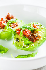 Stuffed avocado halves with sun-dried tomatoes and basil on white plate. Healthy vegan food concept.