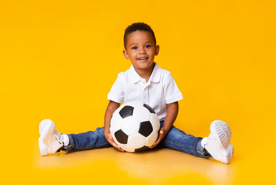 Portrait of cute little boy with soccer ball sitting over yellow studio background