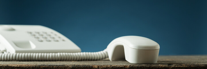 Wide view image of white landline telephone handset of the hook