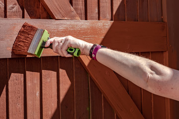 Woman seen painting a timber built gated entrance with a large, timber paintbrush. This shallow focus image is of the paint brush itself as it paints in a horizontal manner,