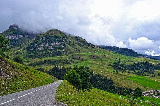La Clusaz, France - August 9th 2017 : Mountain landscape taken near the hamlet la Clusaz, at 10 km of Albertville city. Focus on a road and wonderful green mountains in background, very cloudy.