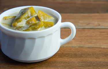 Yummy pumpkin in sweet coconut milk in white bowl, popular Thai dessert on wooden background